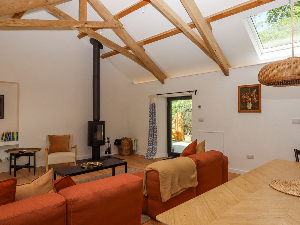 A living room with exposed wooden beams a wood burning stove orange sofas a chair and a door leading outside at 3 Caddaford Barns Buckfastleigh
