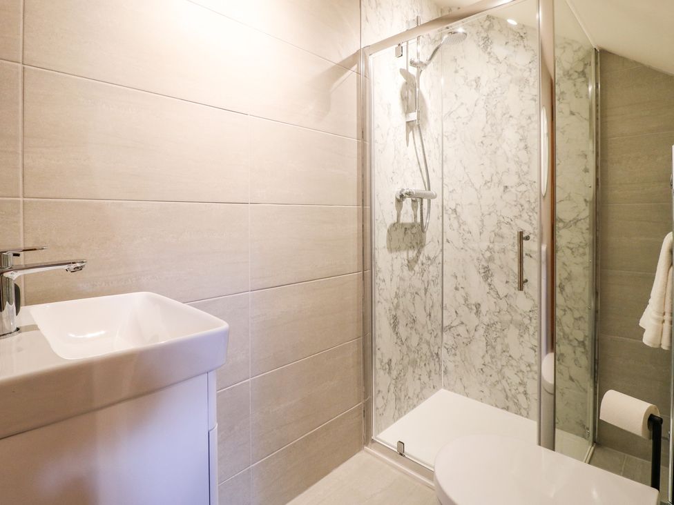 A bathroom with a white sink, shower with glass doors, and a toilet at Rowtor in Birchover