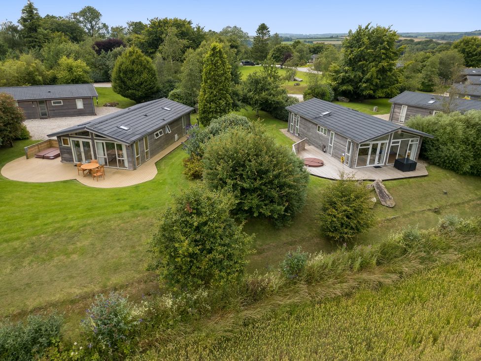 Two wooden cabins with decks and outdoor furniture surrounded by trees and grass at 11 Meadow Retreat in Dobwalls