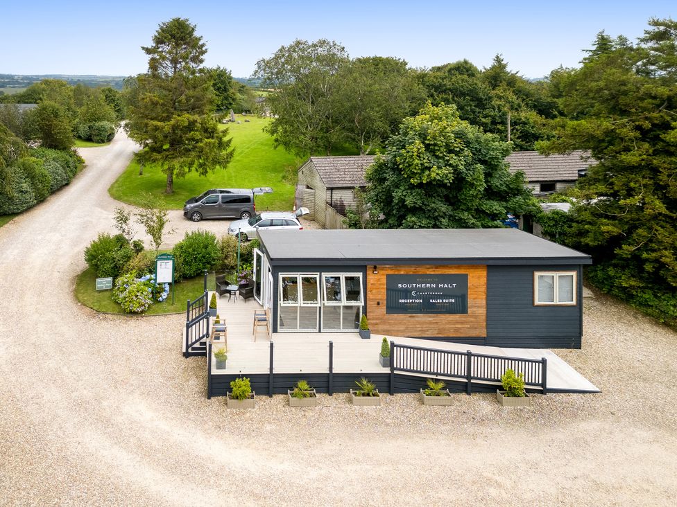 A small building with a deck and ramp in a gravel parking area with cars and trees at 11 Meadow Retreat in Dobwalls