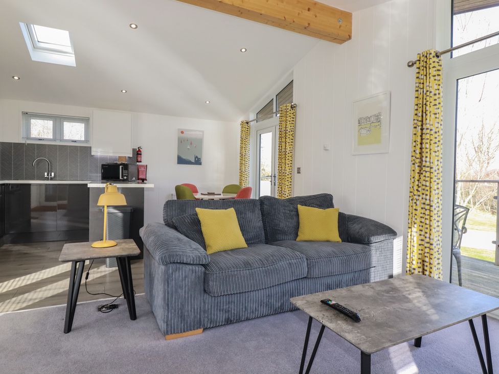 A living room with a gray sofa and yellow pillows a side table with a yellow lamp a coffee table a kitchen area with cabinets and a microwave and a dining table with chairs at 11 Meadow Retreat in Dobwalls
