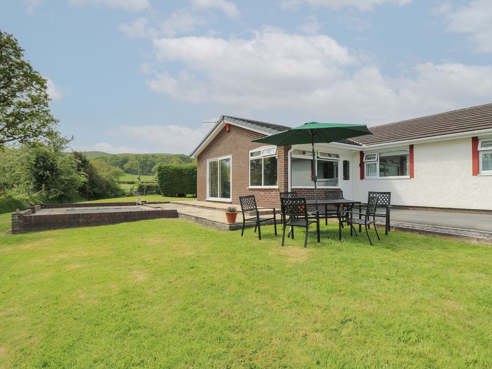A garden with a table umbrella and chairs beside a single story house at Erwlon in Rhydyfelin near Aberystwyth