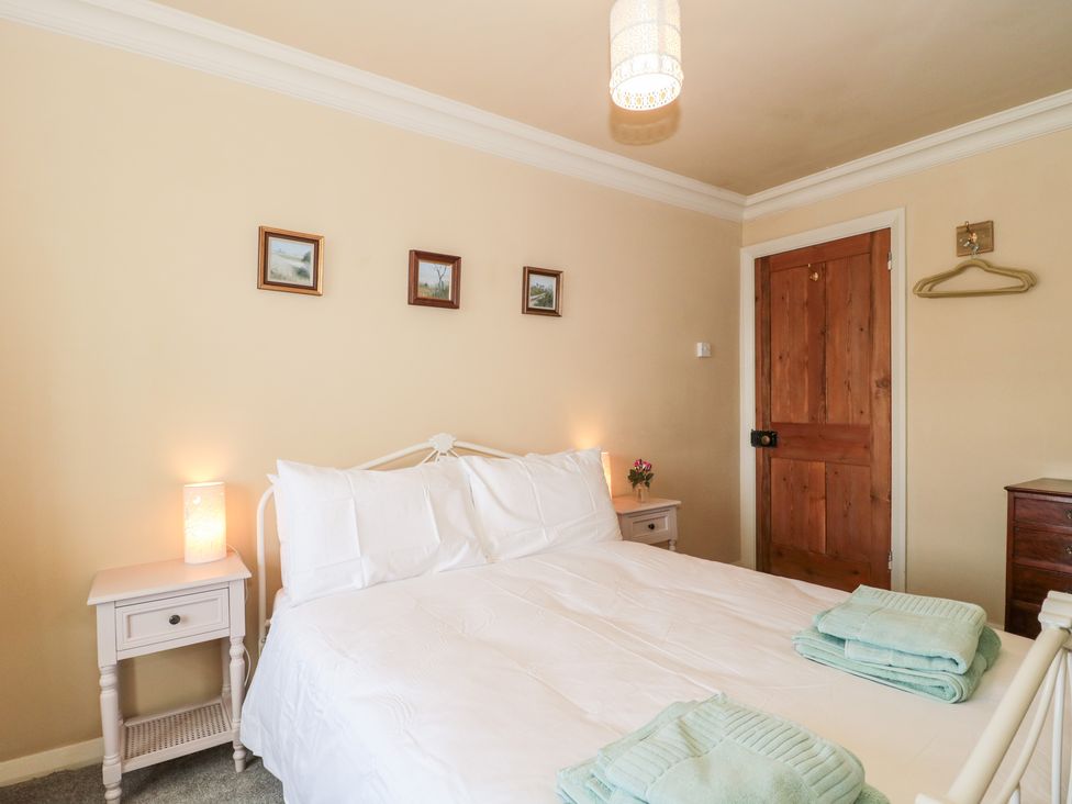 A bedroom with a white bed, bedside tables with lamps, three small framed pictures on the wall, a wooden door, and folded towels on the bed at The Pound in Porlock