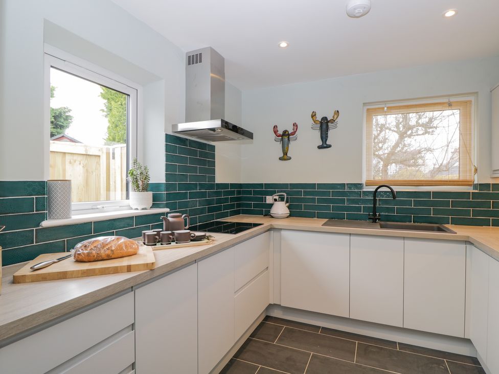 A modern kitchen with white cabinets green tiled backsplash and a wooden countertop at Birch House in Corsham