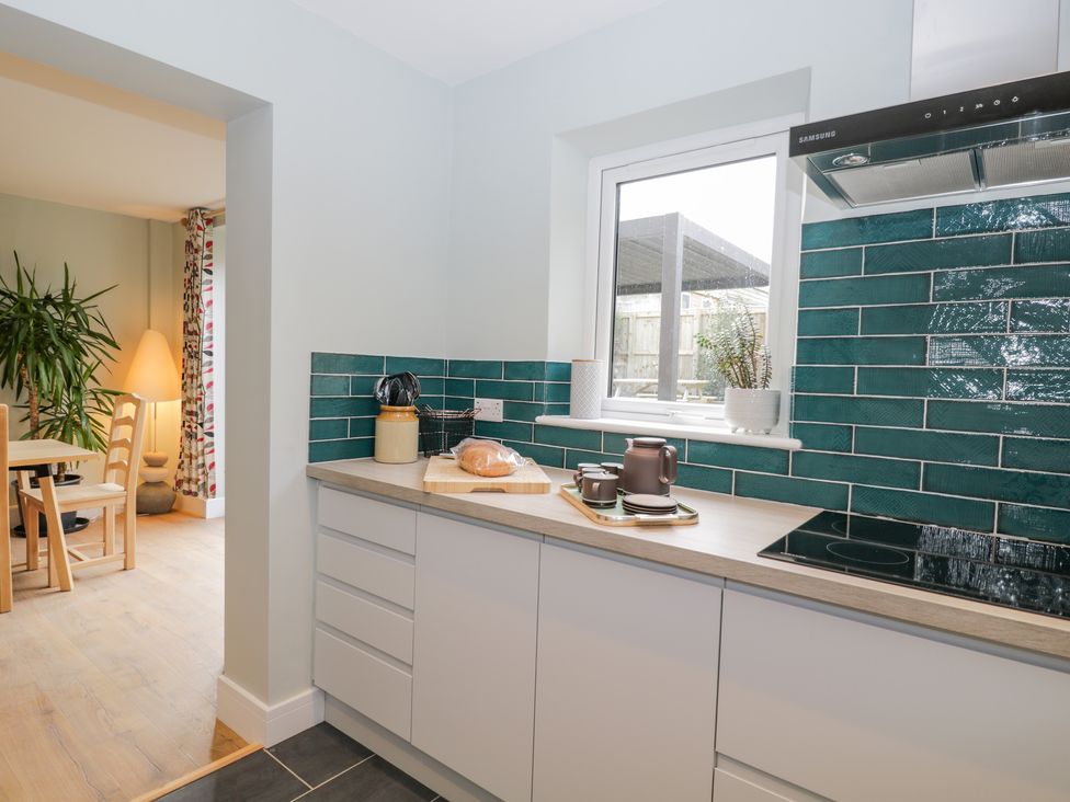 A kitchen counter with green tiled backsplash a window and a dining area visible through an opening at Birch House in Corsham