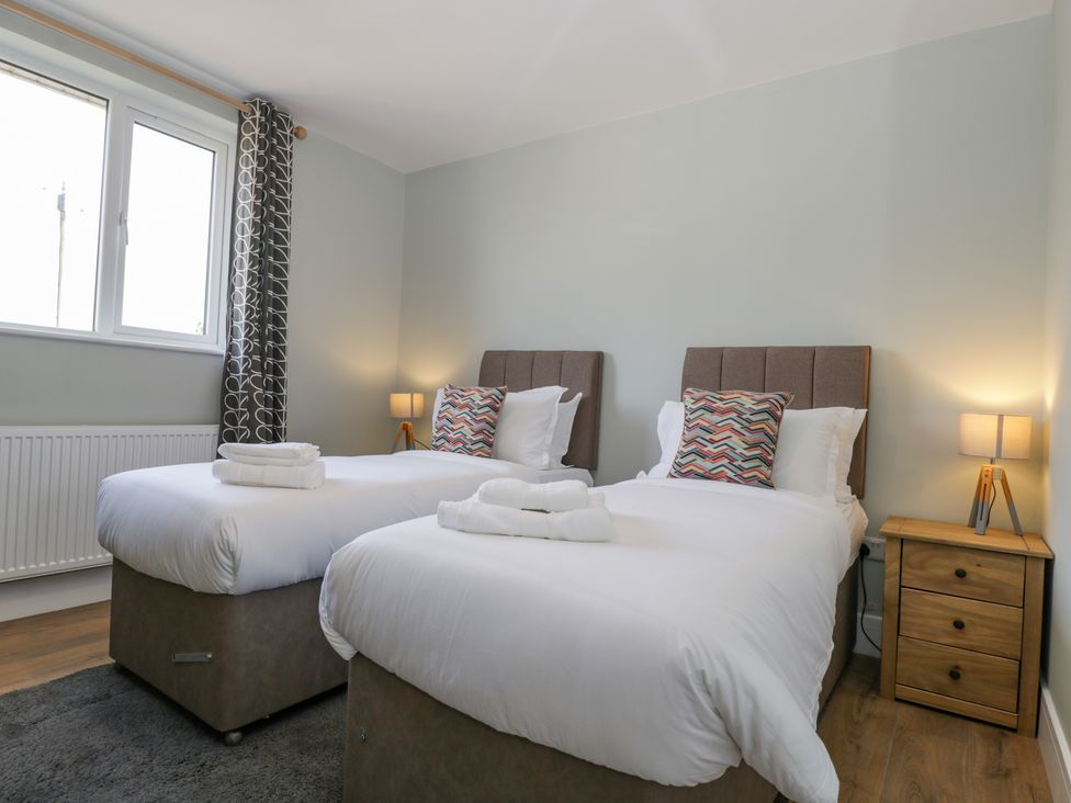 A bedroom with two single beds with white linens colorful pillows wooden nightstand lamps and a window with patterned curtains at Birch House in Corsham