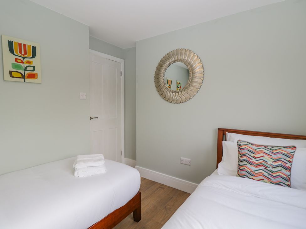 A bedroom with two single beds white bedding a circular mirror on the wall and a door at Birch House in Corsham