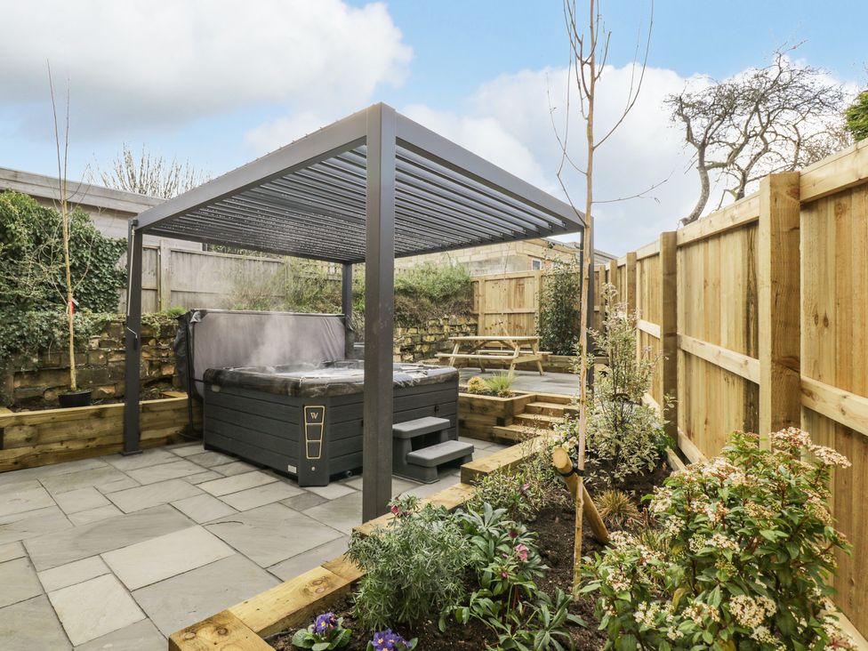 A garden with a hot tub under a pergola wooden fencing and a picnic table at Birch House in Corsham