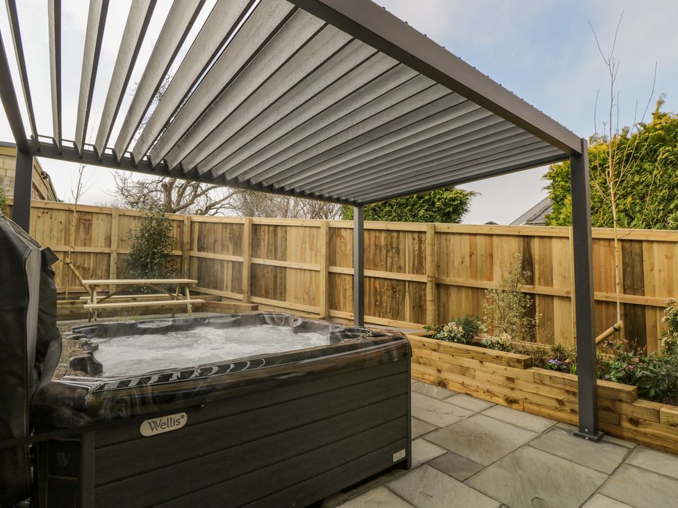 An outdoor area with a hot tub under a pergola and a wooden fence with plants at Birch House in Corsham