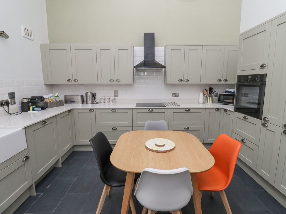 A kitchen with gray cabinets a wooden table and four chairs in black gray white and orange at Coral Cottage in Bamburgh
