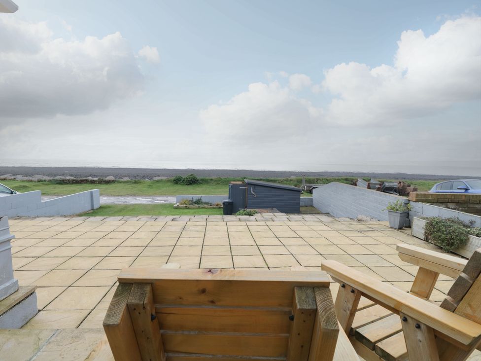 A tiled patio with wooden chairs overlooking a grassy area and a stone beach at The Chalet in Coulderton near Egremont Cumbria