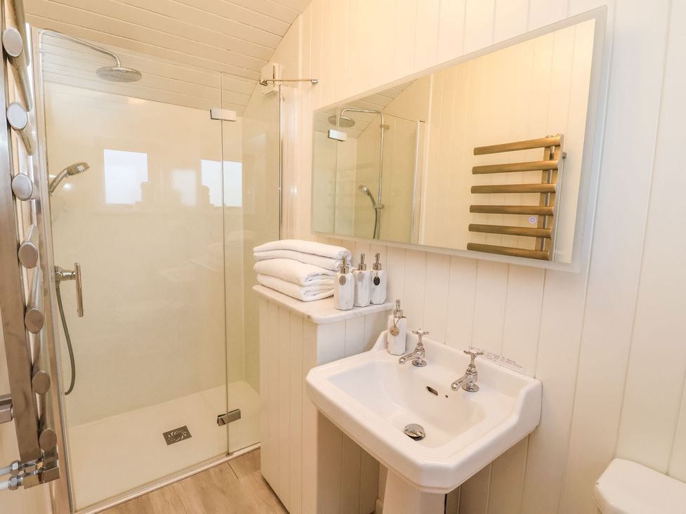 A bathroom with a glass shower enclosure a sink with two taps towels and soap dispensers at The Storyteller in Bolton Percy near Tadcaster