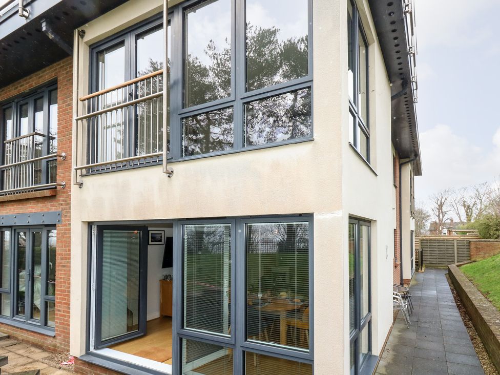 An exterior view of a two-story building with multiple large windows and a patio door opening to a paved walkway at Pointers View in Weymouth