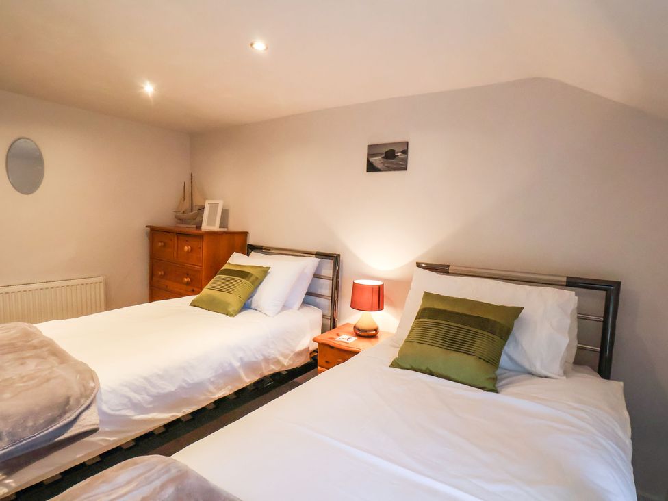 A bedroom with two single beds with green pillows a wooden chest of drawers and a bedside table with a lamp at The Old Sweet Shop in Grosmont
