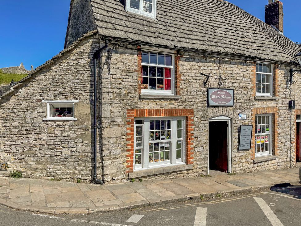 A stone building with windows a door and a sign for Village Bakery at Lodge 6 Corfe Castle