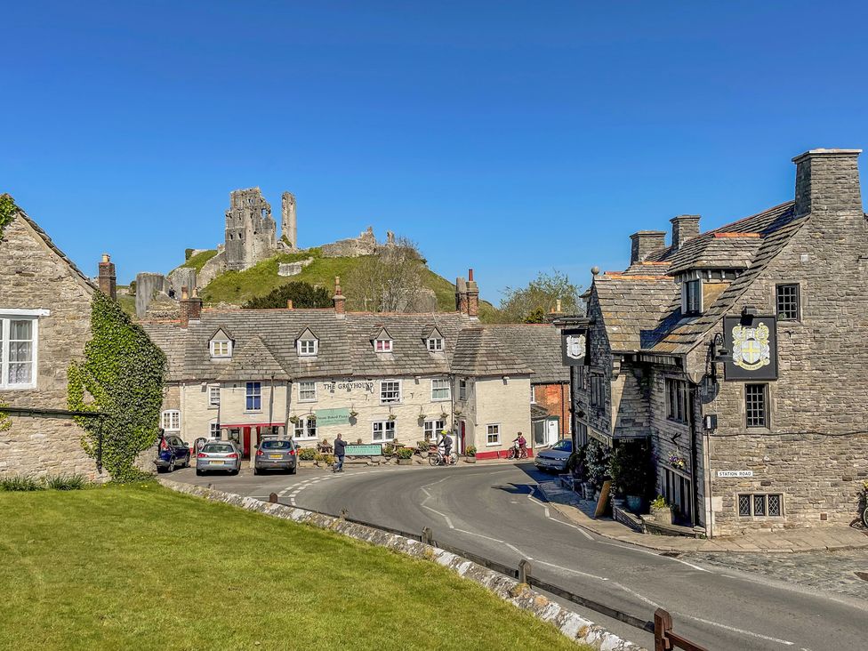 A curved road with stone buildings and a castle ruin on a hill in the background at Lodge 6 in Corfe Castle