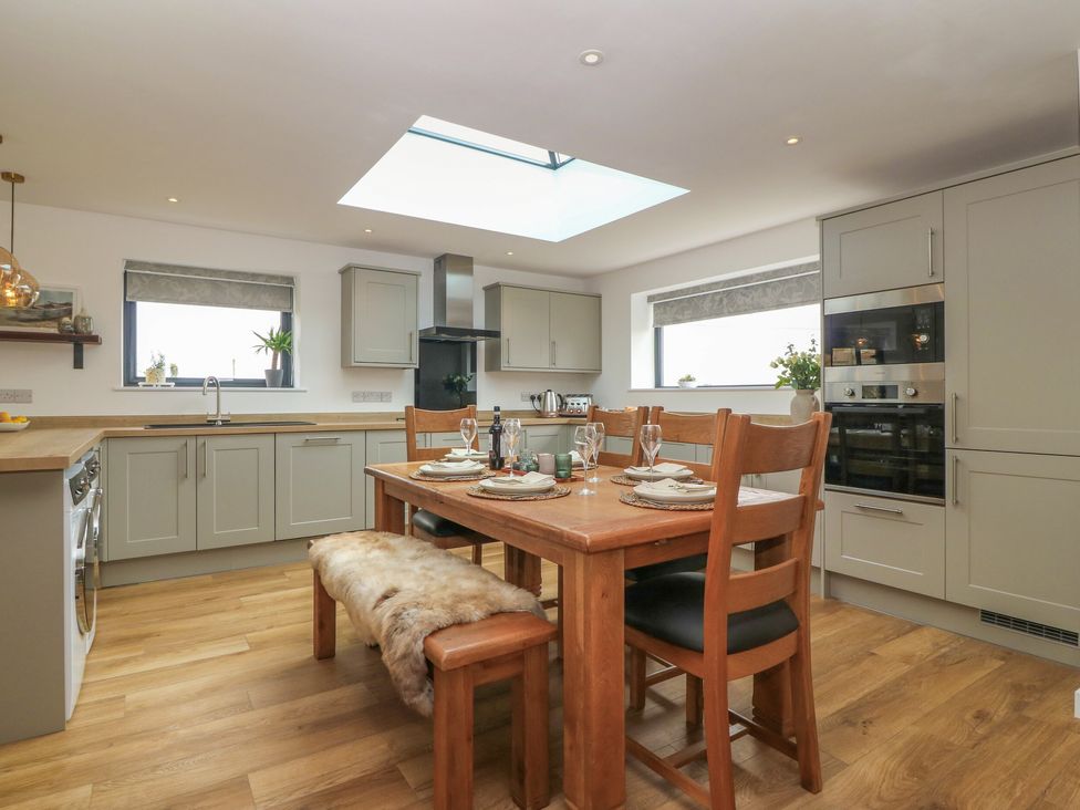 A kitchen with grey cabinets a wooden dining table with plates and glasses and a skylight at Refail Fach Near Cemaes Bay