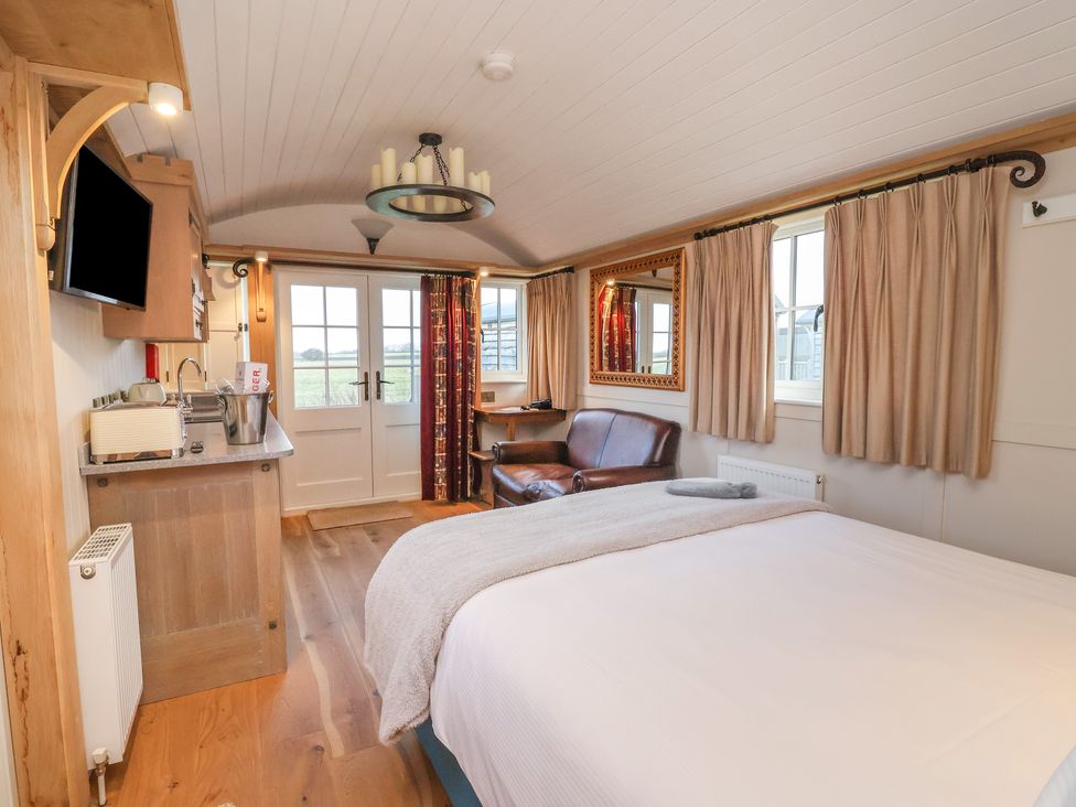 A bedroom with a bed a leather sofa a wall mirror curtains and a kitchenette at The White Princess in Bolton Percy near Tadcaster