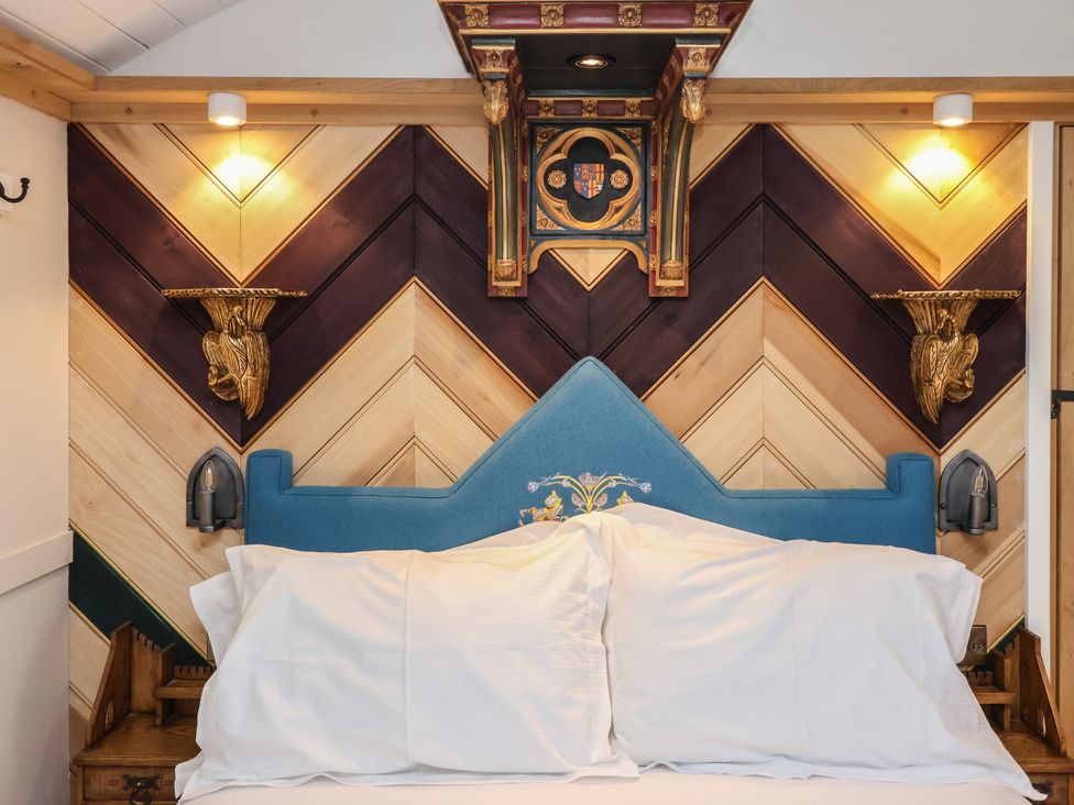 A bed with a blue headboard and white pillows against a wood paneled wall with golden wall sconces at The White Princess in Bolton Percy near Tadcaster