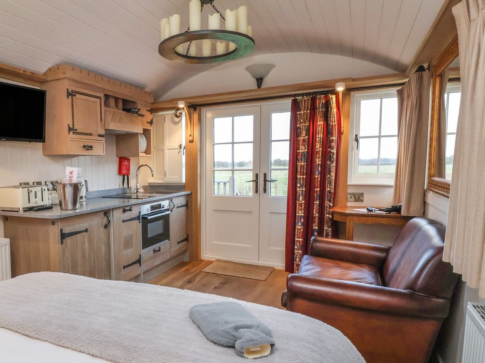 A compact kitchen with wooden cabinets next to a brown leather sofa and double doors with a window at The White Princess Bolton Percy near Tadcaster