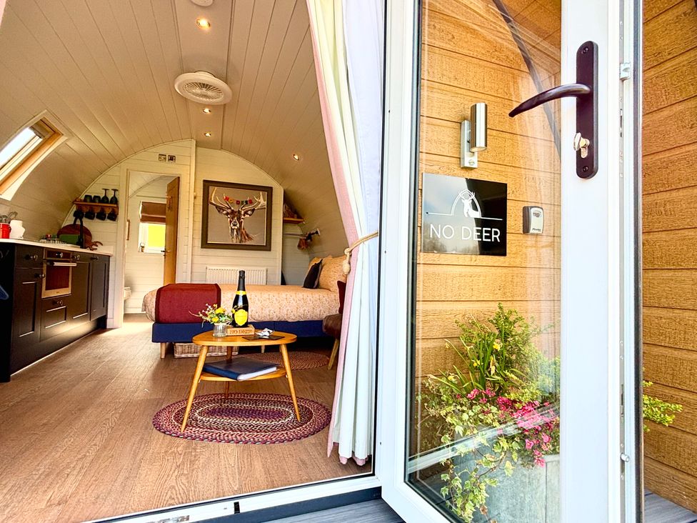 A small bedroom with a bed a round wooden table with a bottle and flowers and a kitchenette at No Deer in Ashbourne