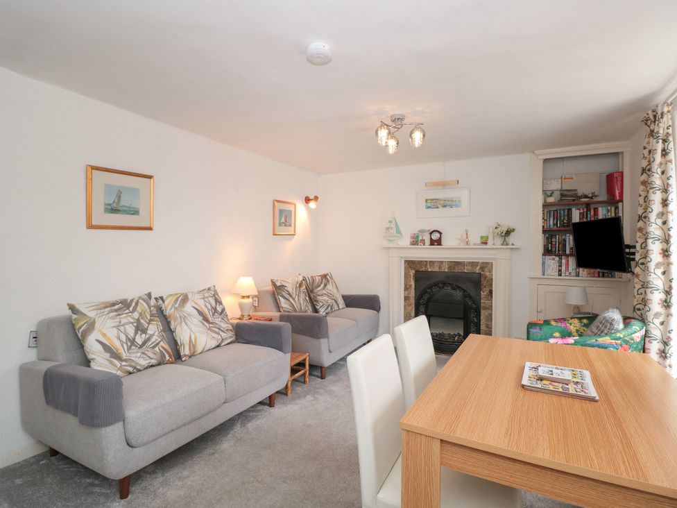 A living room with two sofas a wooden dining table with chairs a fireplace and a bookshelf at Dart Cottage in Dittisham