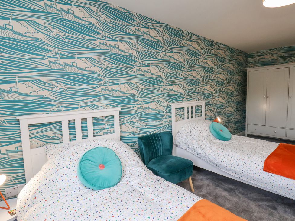 A bedroom with two single beds a teal chair and a wardrobe at Whitby Waves in Whitby