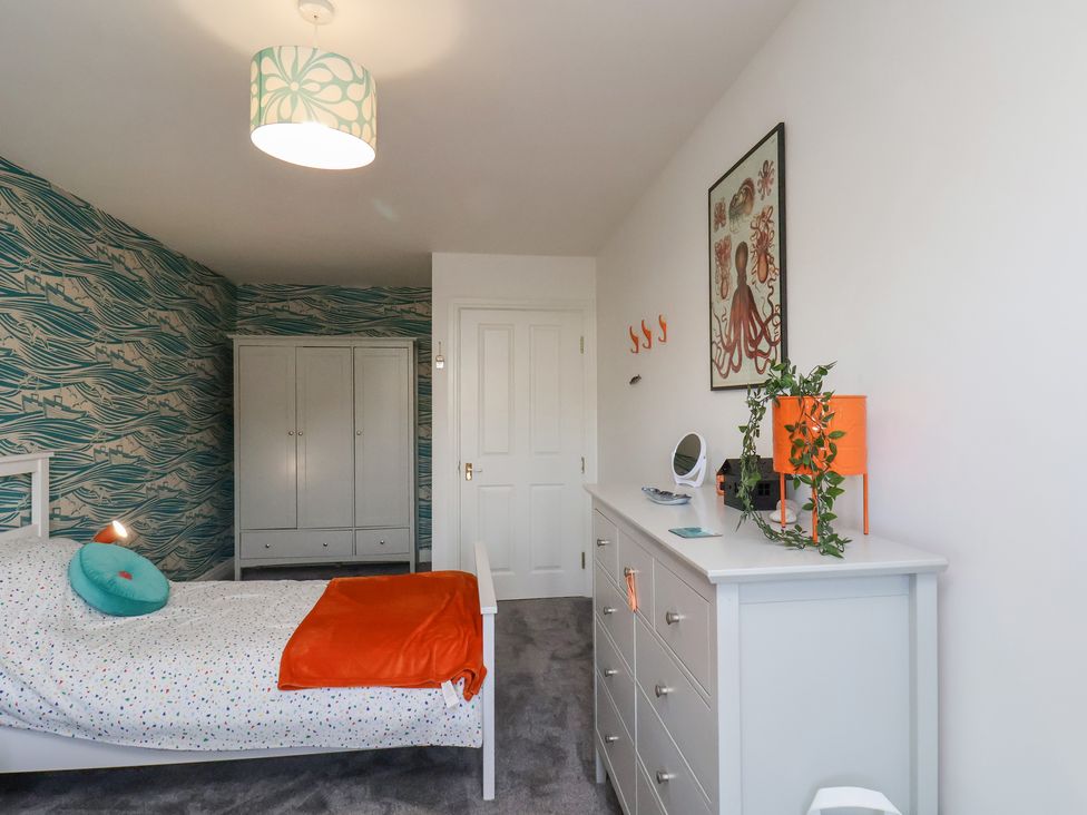 A bedroom with a single bed with a patterned duvet and an orange blanket a chest of drawers with a plant and decorations a wardrobe and a door at Whitby Waves in Whitby