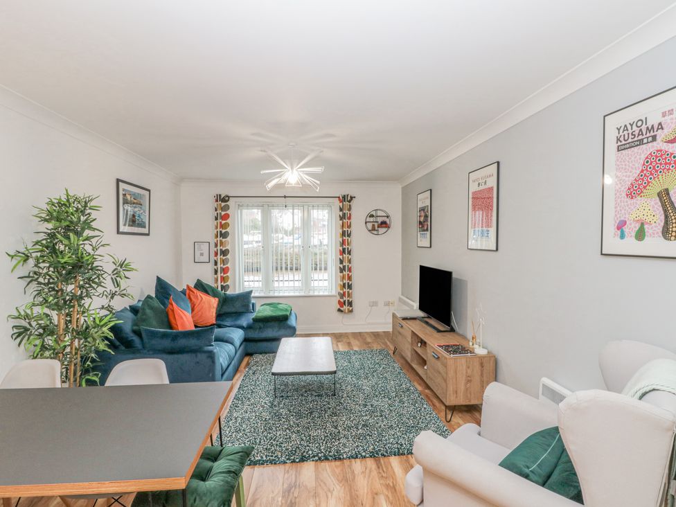 A living room with a blue sofa, wooden coffee table, TV on a wooden stand, and dining table with chairs at Whitby Waves in Whitby