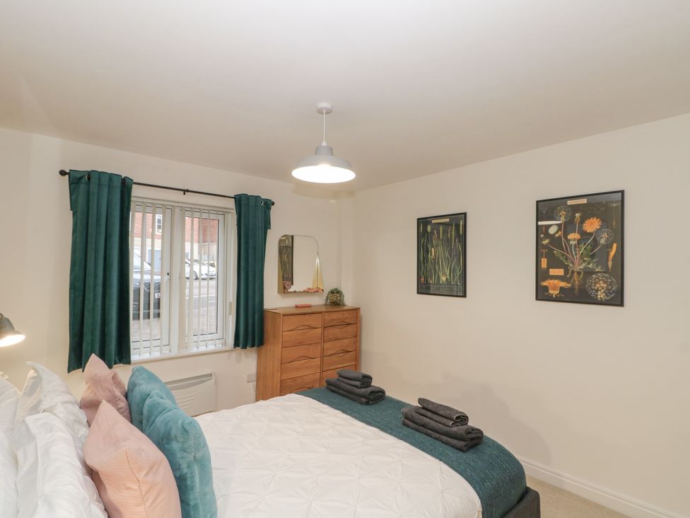 A bedroom with a bed and pillows a wooden chest of drawers with a mirror green curtains and framed botanical prints on the wall at Whitby Waves in Whitby