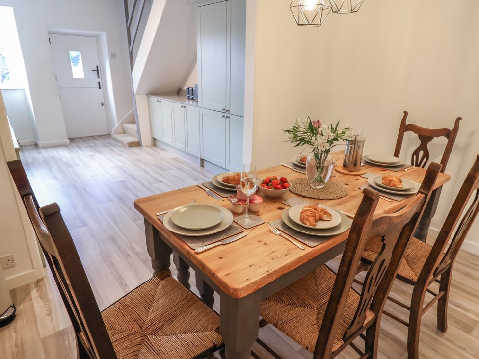 A dining area with a wooden table and chairs set with plates croissants and strawberries in a room with light wood flooring at Ribble Cottage in Settle