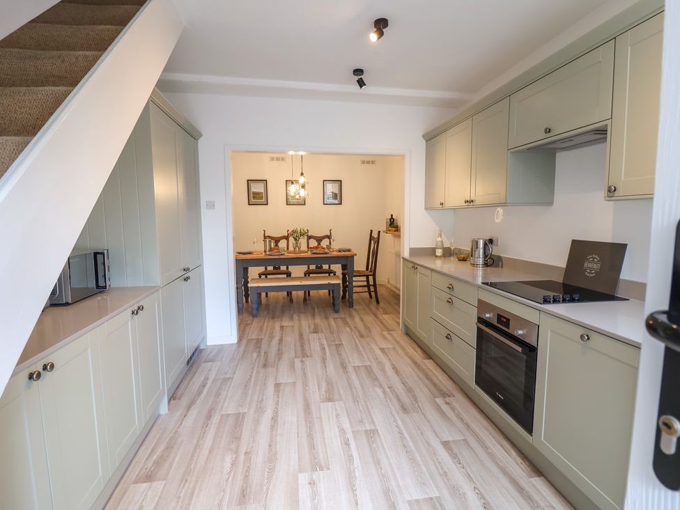 A kitchen with green cabinets a stove and oven and a dining room with a table and chairs at Ribble Cottage in Settle