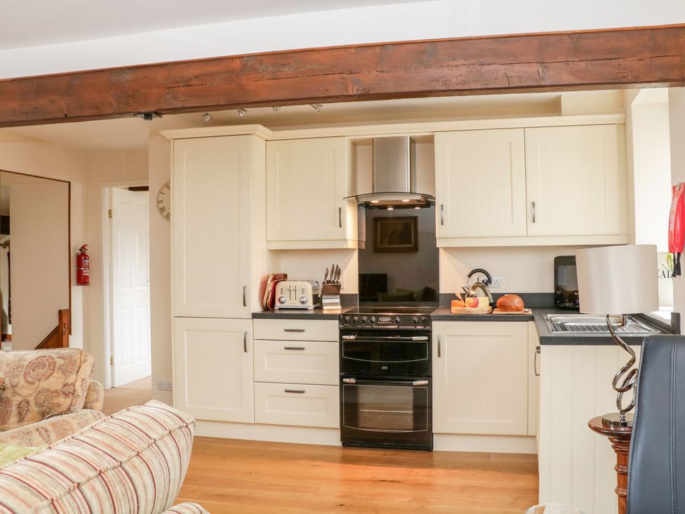 A kitchen with cream cabinets, a black oven, toaster, kettle, bread, and a lamp on a counter at The Hayloft at Tennant Barn in Malham
