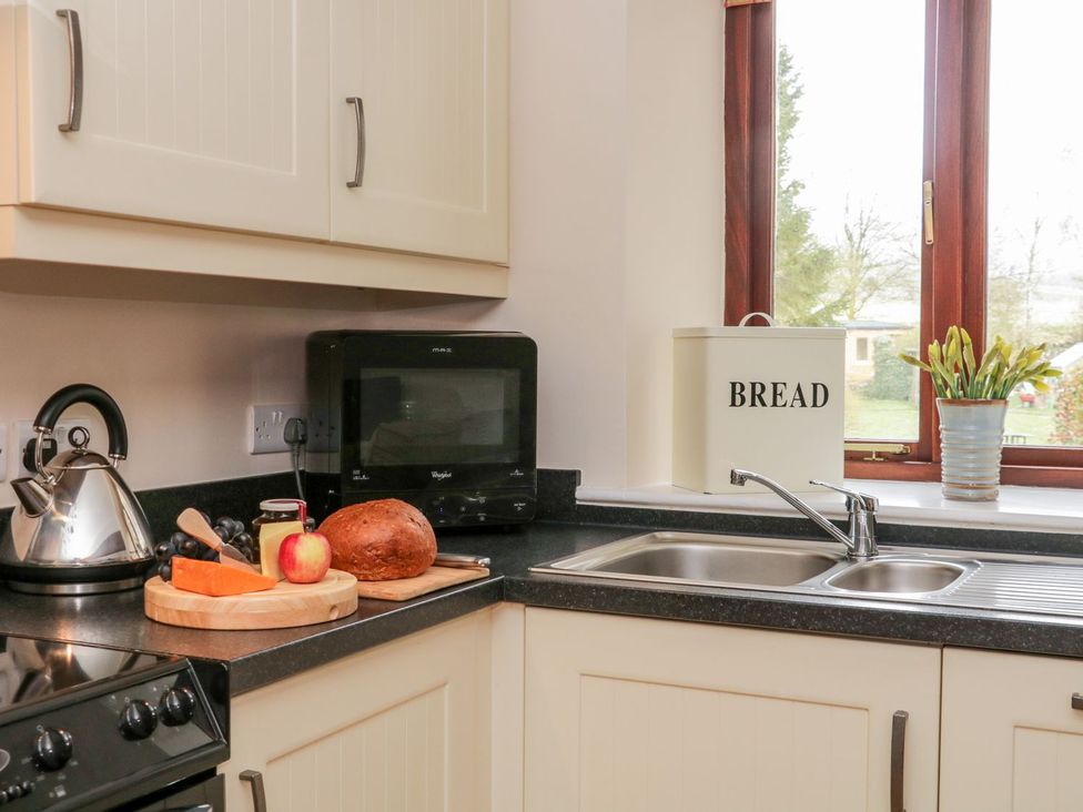 A kitchen corner with a sink under a window a bread bin a microwave a kettle and a cutting board with bread cheese an apple and grapes on the counter at The Hayloft at Tennant Barn in Malham