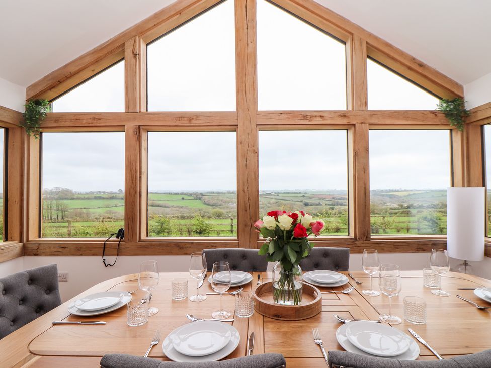 A dining room with wooden table and grey chairs overlooking a countryside view at Trevilges Cottage Trewennack near Helston