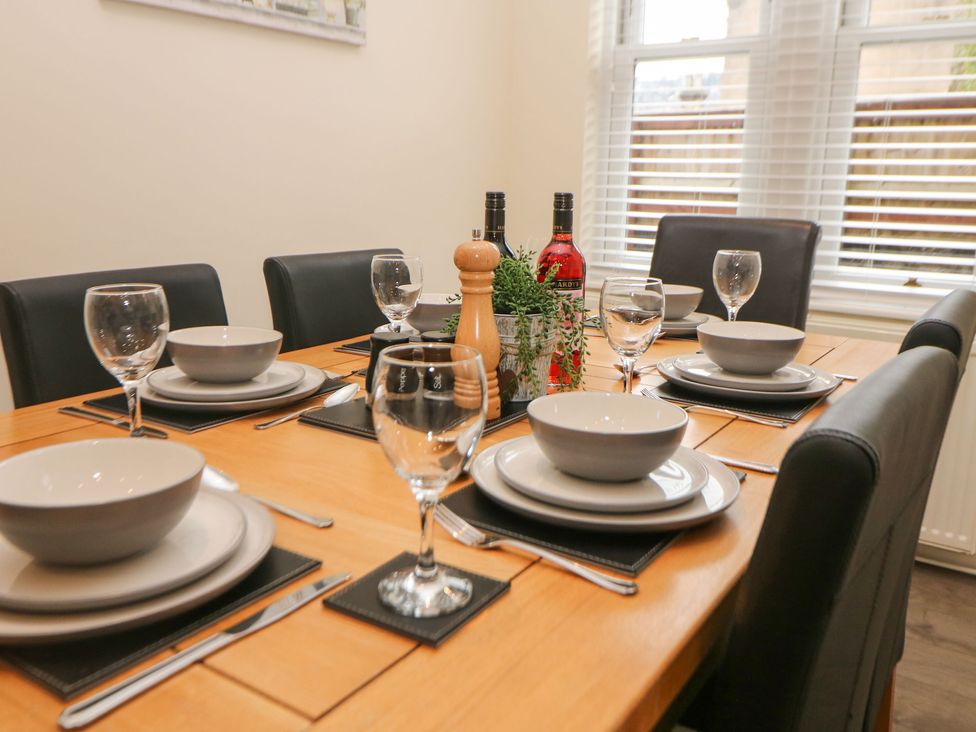 A dining table set with bowls plates glasses and cutlery with wine bottles and a plant at 1 Knowleston House in Matlock
