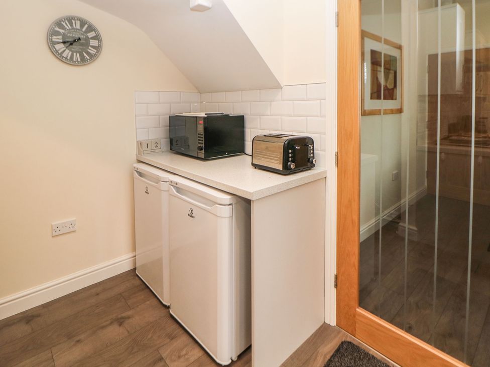 A small kitchen area with two white under-counter fridges a microwave and a toaster on the countertop and a wall clock above at 1 Knowleston House in Matlock