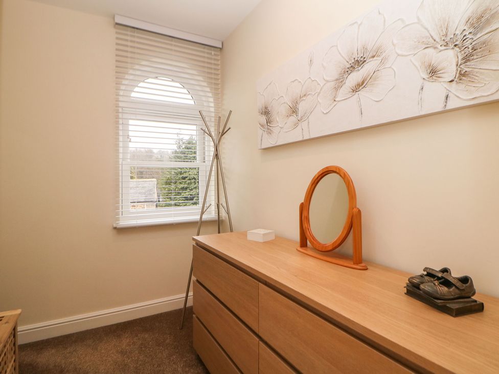 A room with a wooden dresser a round mirror a coat rack and a window with blinds at 1 Knowleston House in Matlock