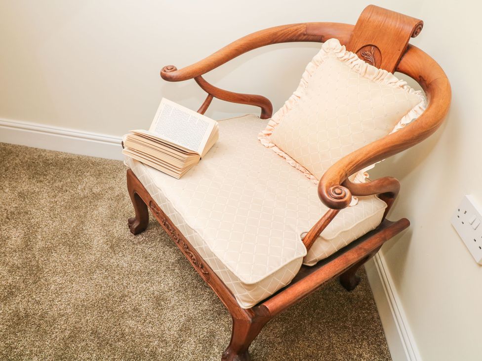 A wooden armchair with beige cushions and an open book on the seat on a carpeted floor at 1 Knowleston House in Matlock