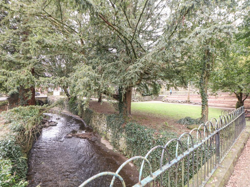 A small river flowing beside a grassy park area with trees and stone walls at 1 Knowleston House in Matlock