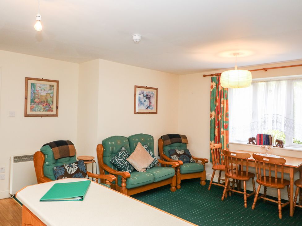 A living room with green cushioned wooden chairs a wooden dining table and chairs and framed pictures on the wall at 2 Garnish Court in Glengarriff County Cork
