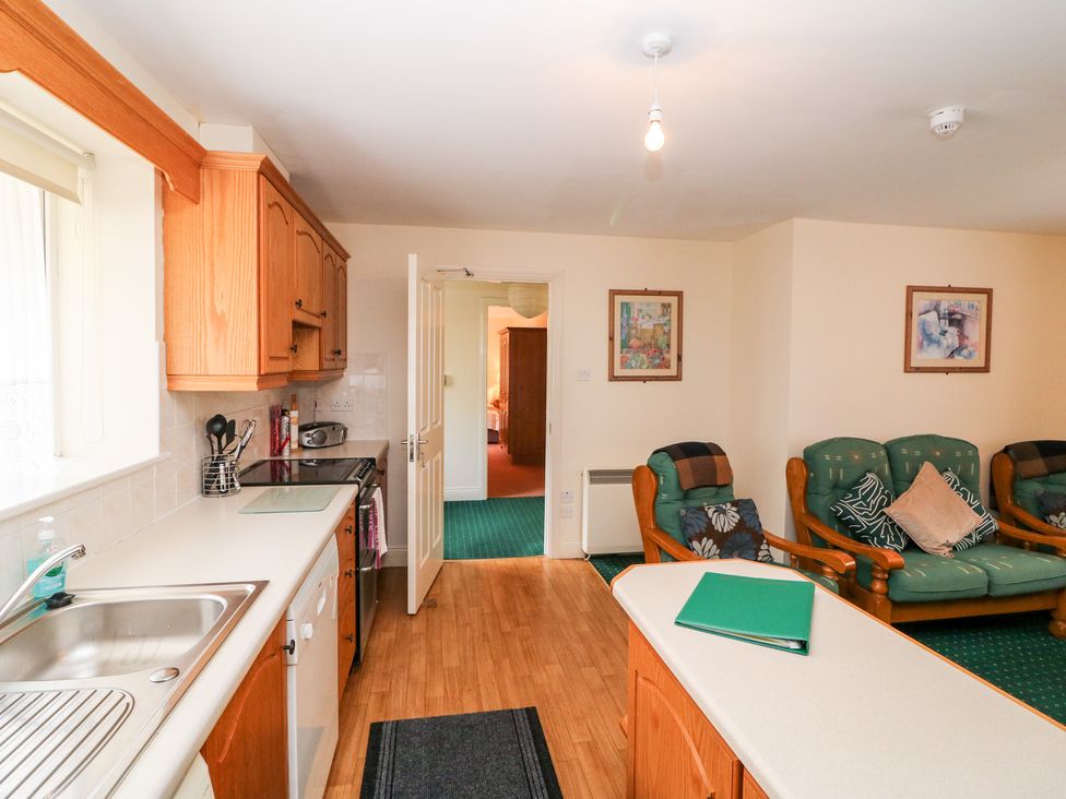 A kitchen and living room with wooden cabinets, green cushioned chairs, and a green binder on the counter at 2 Garnish Court in Glengarriff County Cork