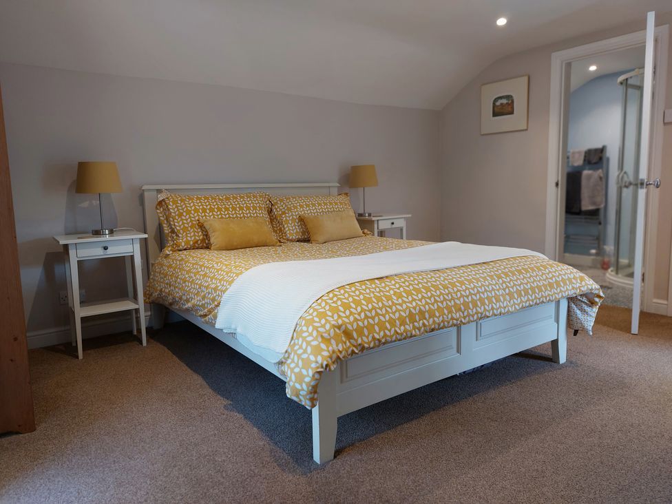 A bedroom with a bed with yellow patterned bedding two bedside tables with lamps and an open door to a bathroom at The Coach House Canonbie near Langholm