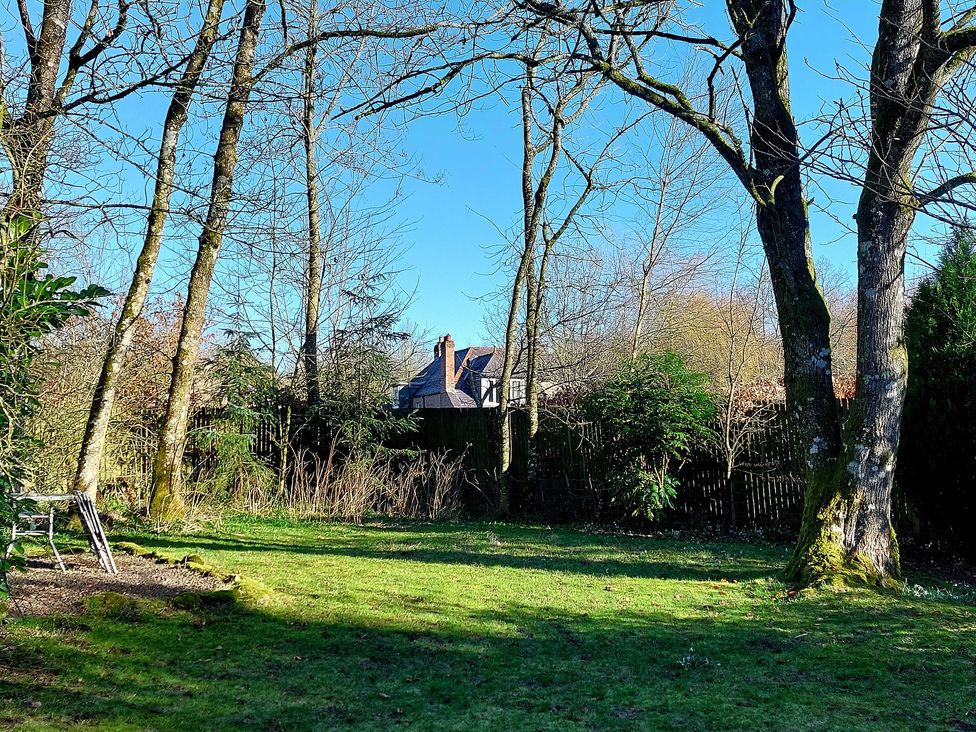 A garden with trees and grass and a house visible behind a fence at The Coach House Canonbie near Langholm