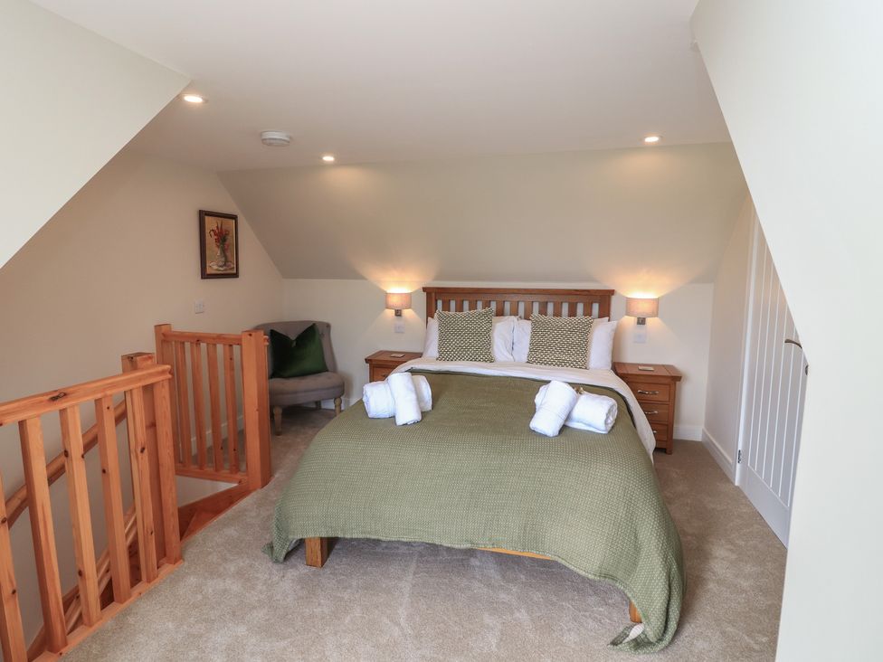 A bedroom with a double bed made with green bedding and rolled white towels two bedside tables with lamps a chair and wooden stair rails at Wee Smithy Munlochy