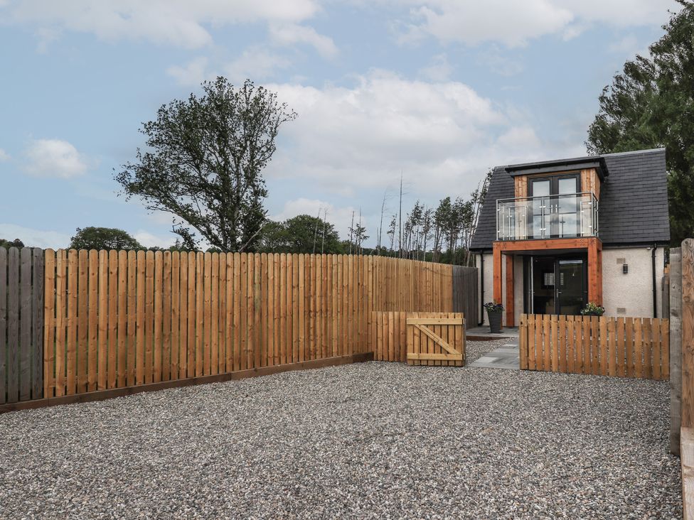 A small two-story house with a balcony and wooden fence around a gravel yard at Wee Smithy in Munlochy