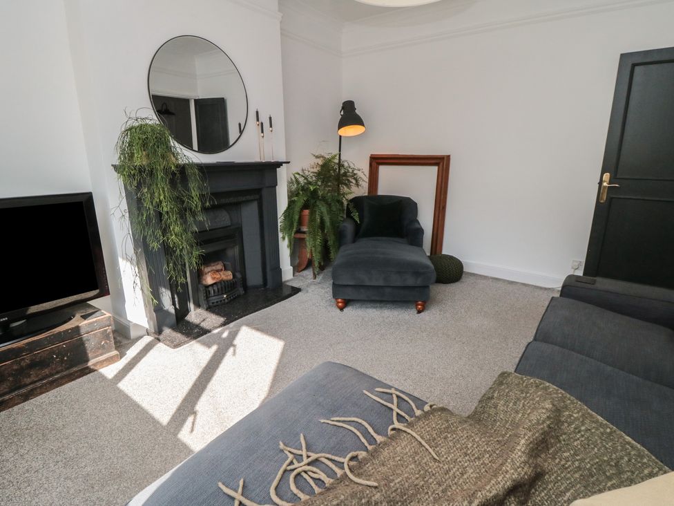 A living room with a black fireplace round mirror chaise lounge plants and a television at Top-Notch Flat in Saltburn-By-The-Sea