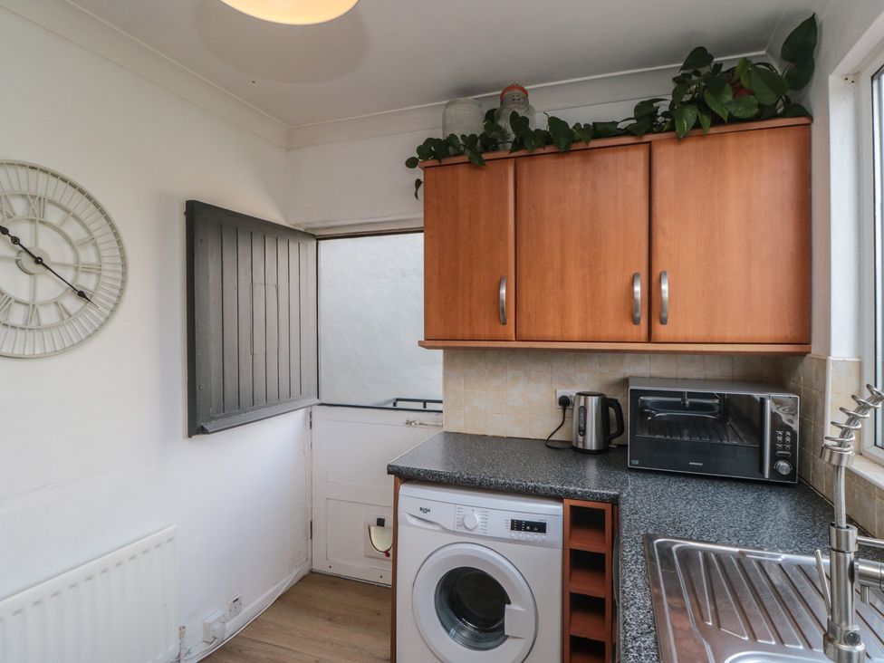 A kitchen with wooden cabinets washing machine kettle toaster and a sink at Top-Notch Flat in Saltburn-By-The-Sea