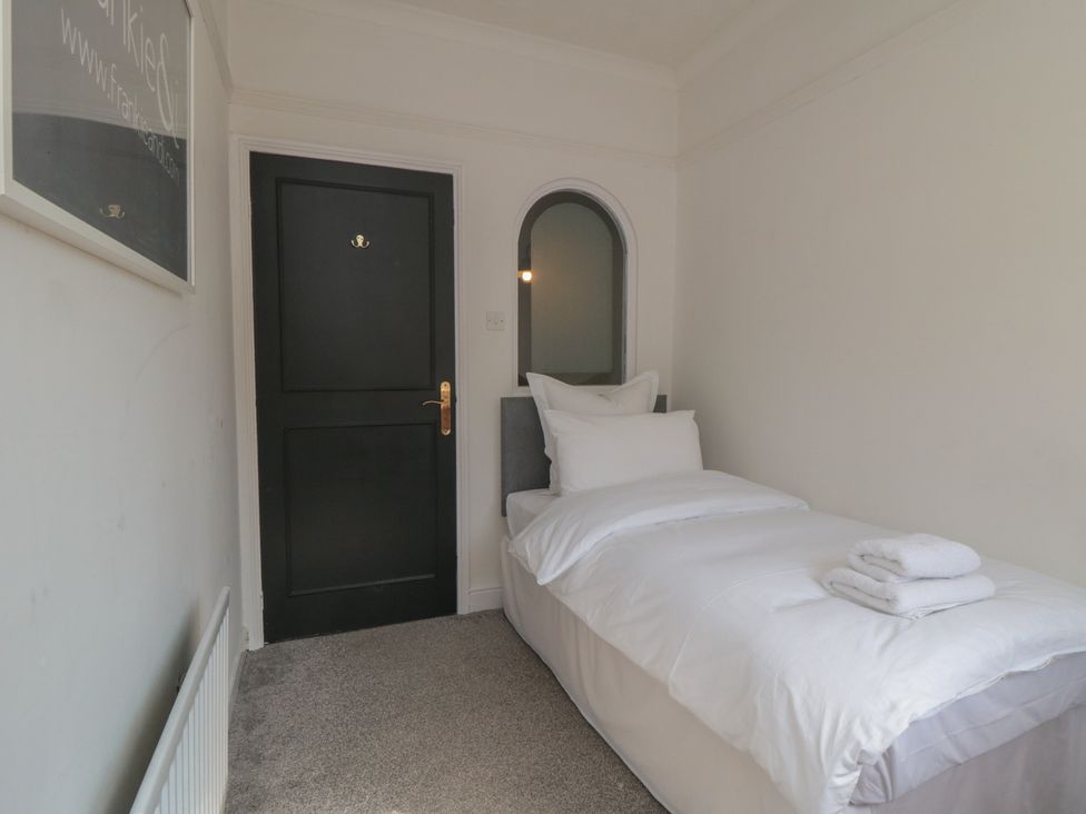 A small bedroom with a single bed next to a black door and a wall mirror at Top-Notch Flat in Saltburn-By-The-Sea