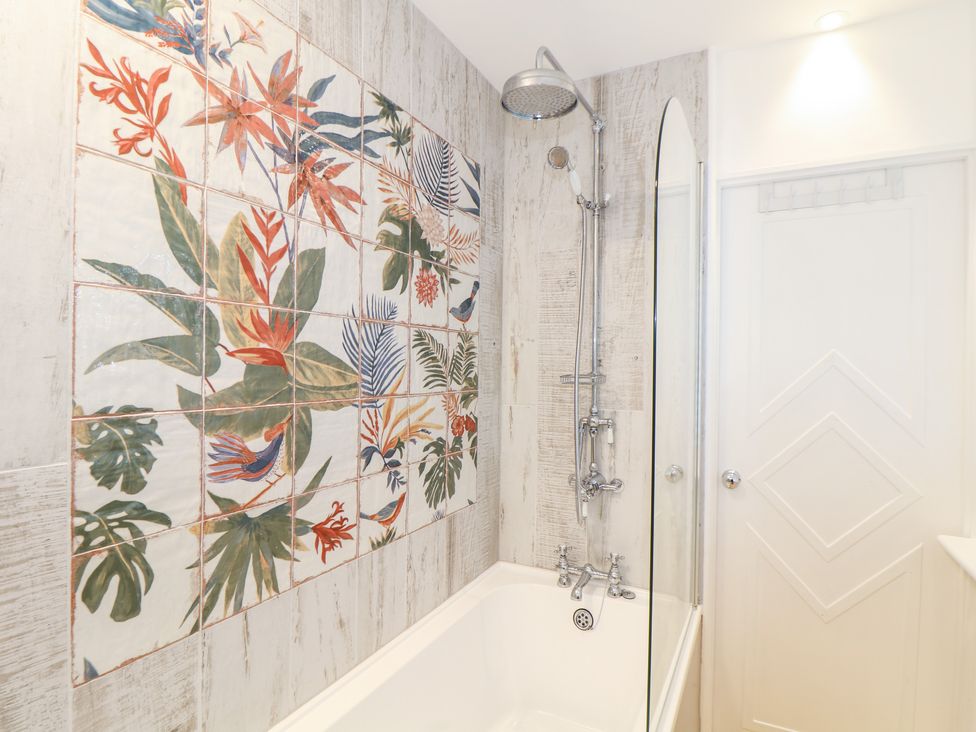 A bathroom with a bathtub shower combination and floral patterned wall tiles at The Hexagon House in Goldsithney